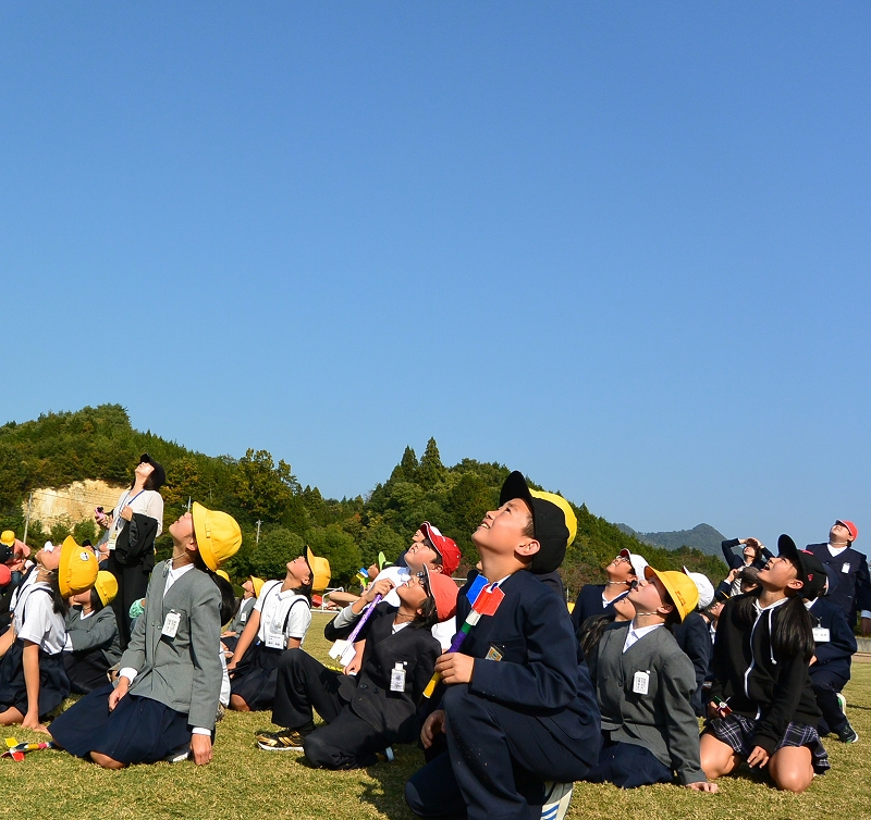 大空高く打ち上がるロケットを見上げる児童